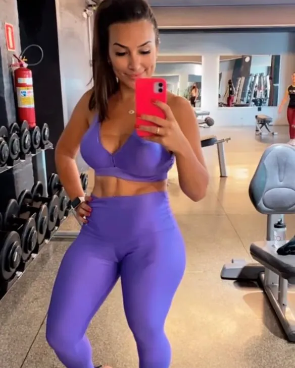 Mulher de top e legging roxos fazendo selfie no espelho da academia