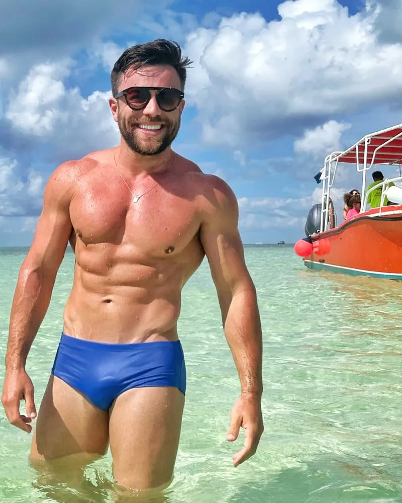Homem sorrindo dentro do mar, com um barco ao fundo
