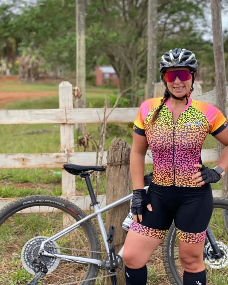 Ciclista de capacete e óculos ao lado da bicicleta, numa fazenda